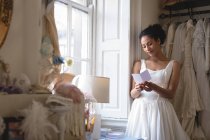 Giovane sposa in abito da sposa leggere una nota alla finestra boutique — Foto stock