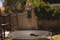 Ragazza che salta su un trampolino in giardino in una giornata di sole — Foto stock