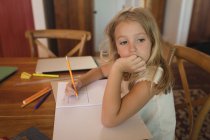 Fille réfléchie faisant ses devoirs à la maison et regardant ailleurs, main sur le menton — Photo de stock
