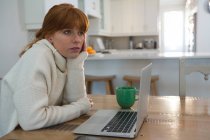 Red hair woman using laptop in kitchen at home — Stock Photo