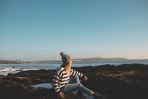 Nachdenkliche Frau sitzt am Strand auf einem Felsen — Stockfoto