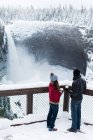 Casal em roupas quentes olhando para cachoeira durante o inverno — Fotografia de Stock