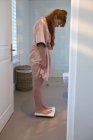 Mujer comprobando su peso en básculas de pesaje en casa - foto de stock