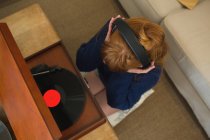 Жінка в навушниках слухає музику на грамофоні вдома — стокове фото