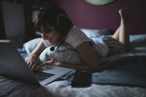 Frau benutzt Laptop mit Headset im heimischen Schlafzimmer — Stockfoto