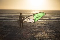 Surfeur masculin debout avec cerf-volant sur la plage au crépuscule — Photo de stock