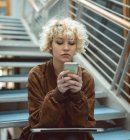 Junge Frau benutzt Handy im Treppenhaus — Stockfoto