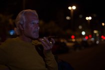 Старший чоловік розмовляє по мобільному телефону в місті вночі — стокове фото