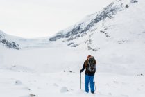 Rückansicht eines männlichen Bergsteigers, der im Winter auf einem schneebedeckten Berg wandert — Stockfoto
