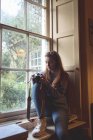 Frau überprüft Bilder auf Retro-Kamera in der Nähe des Fensters zu Hause — Stockfoto