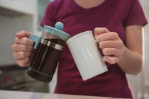 Partie médiane de la femme versant du café noir dans une tasse dans la cuisine à la maison — Photo de stock