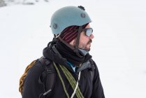Thoughtful male mountaineer standing with helmet and sunglasses on a snowy region — Stock Photo