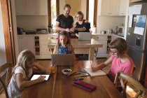 Родители используют ноутбук, когда дети учатся на кухне дома — стоковое фото