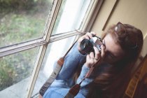 Женщина фотографируется с ретро-камерой у окна дома — стоковое фото