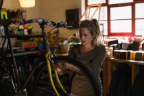 Young female mechanic fixing bicycle in workshop — Stock Photo