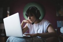 Mulher usando laptop com fone de ouvido no quarto em casa — Fotografia de Stock