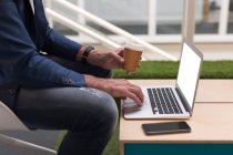 Imagem cortada de empresário que toma café enquanto usa laptop no escritório — Fotografia de Stock