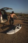 Surfista maschile con tavola da surf in spiaggia in una giornata di sole — Foto stock