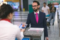 Atendente de check-in de linha aérea verificando bilhete de pensionista em tablet digital no aeroporto — Fotografia de Stock
