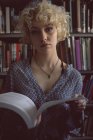 Portrait of young woman holding a book in library — Stock Photo