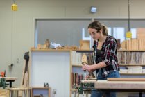 Carpinteiro feminino usando cinzel com martelo em um pedaço de madeira na oficina — Fotografia de Stock