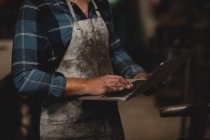 Mid section of blacksmith using laptop in workshop — Stock Photo