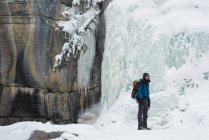 Bergsteiger steht im Winter in der Nähe von felsigen Bergen — Stockfoto