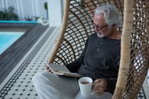 Активний старший чоловік читає книгу, сидячи на гойдалці — стокове фото