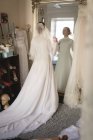 Кавказская невеста в свадебном платье и вуали, смотрящая в зеркало в винтажном бутике — стоковое фото