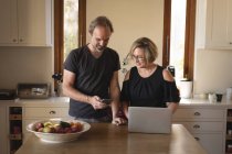 Пара за допомогою мобільного телефону та ноутбука на кухні вдома — стокове фото