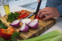 Sección media del hombre cortando verduras en la cocina en casa - foto de stock