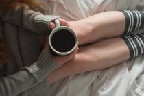 Donna che tiene in mano tazza di caffè nero in camera da letto a casa — Foto stock