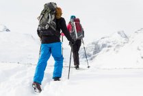 Задний вид на пару, идущую по заснеженной горе зимой — стоковое фото