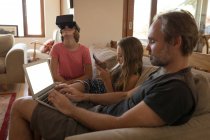Pai e filhas usando dispositivos eletrônicos na sala de estar em casa — Fotografia de Stock