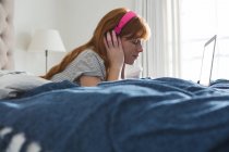 Femme avec écouteurs écoutant de la musique dans la chambre à coucher à la maison — Photo de stock