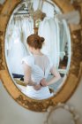 Отражение в зеркале рыжих волос невесты, регулирующей свадебное платье молнией на спине — стоковое фото