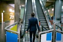 Empresário caminhando com bagagem em direção escada rolante no aeroporto — Fotografia de Stock