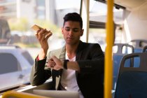 Empresário verificando o tempo enquanto fala no celular no ônibus — Fotografia de Stock