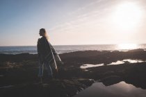 Жінка ходить по скелі на пляжі під час заходу сонця — стокове фото