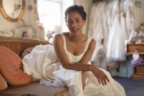 Schöne Mischlingsbraut im Brautkleid auf dem Sofa sitzend — Stockfoto