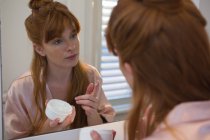 Женщина наносит крем на лицо в ванной комнате дома — стоковое фото