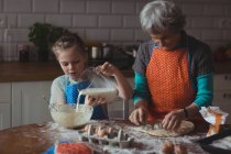 Abuela y nieta preparando galletas en la cocina en casa - foto de stock