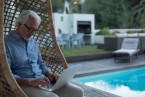 Uomo anziano attivo utilizzando laptop vicino a bordo piscina — Foto stock