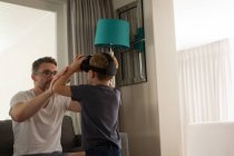 Father helping his son in using virtual reality headset in living room at home — Stock Photo