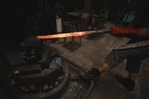 Кузнец формирует горячий металлический стержень в машине в мастерской — стоковое фото