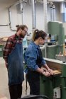 Carpinteiros masculinos e femininos trabalhando juntos na máquina de corte vertical na oficina — Fotografia de Stock