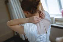 Rear view of bride adjusting button on back of wedding dress in boutique — Stock Photo