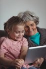 Grand-mère et petite-fille utilisant une tablette numérique dans le salon à la maison — Photo de stock