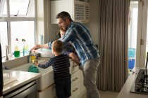Padre e hijo fregadero de limpieza en la cocina en casa - foto de stock