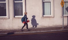 Donna che cammina con zaino e skateboard su un sentiero in città — Foto stock
